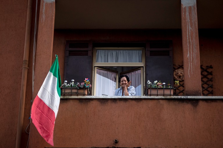 A woman with the Italian flag looks out of her balcony, Rome