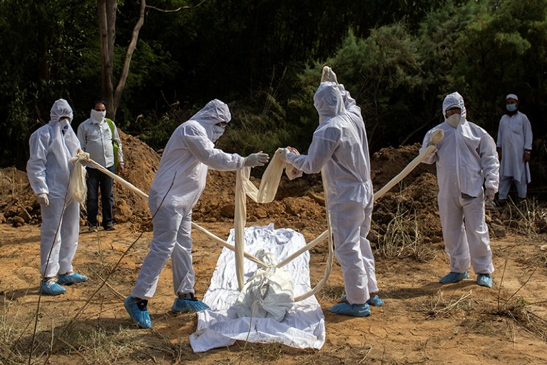 Relatives wearing protective gear prepare to bury the body of a COVID-19 victim in New Delhi, India