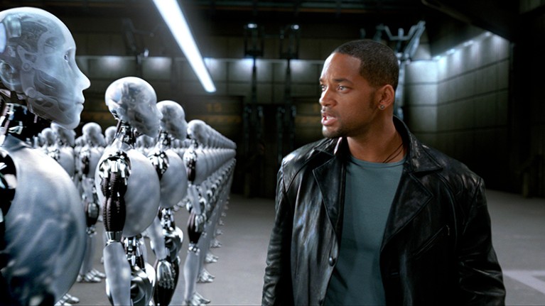 Will Smith looks angrily at lines of translucent robots in a warehouse.