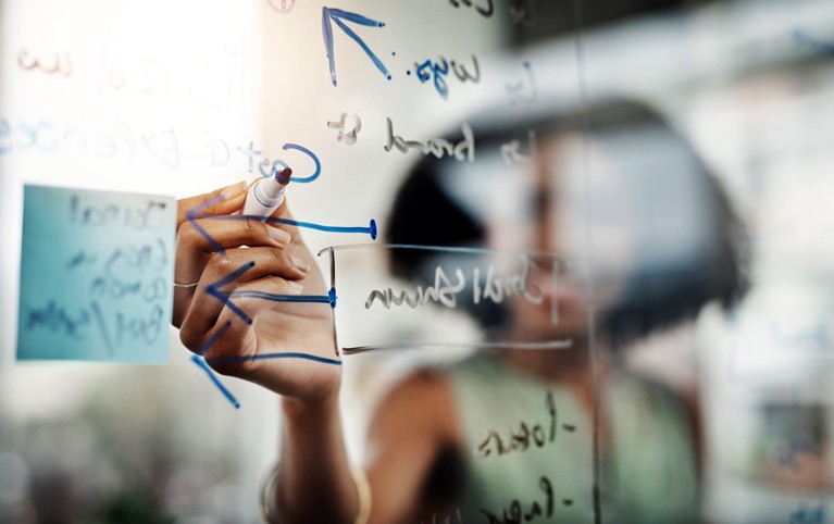 Sun shining behind a woman writing on a transparent glass wipe board