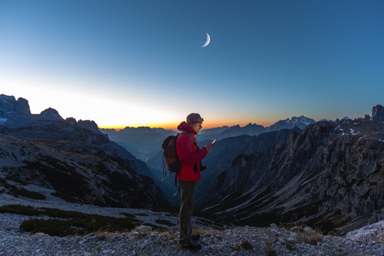 A hiker in the mountains at sunset checks a mobile device.