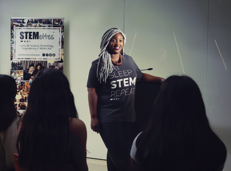 Anne Marie Imafidon stands at a lectern wearing a t-shirt that reads "Eat Sleep STEM Repeat"