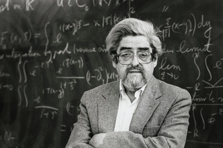 A black and white photograph of Louis Nirenberg standing in front of a blackboard circa 1991