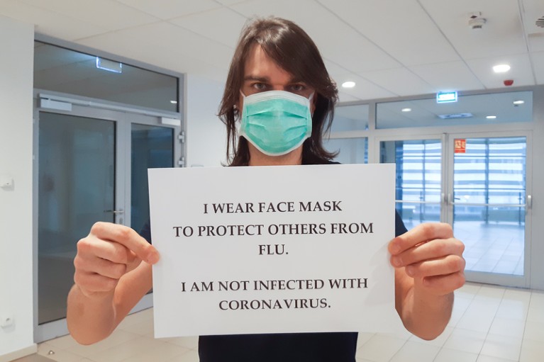 Dr. Piotr Rzymski wearing a face mask and holding a sign that reads: 'I am not infected with coronavirus'
