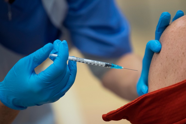 A close up of syringe containing the Pfizer-BioNTech vaccine as it is administered to a man