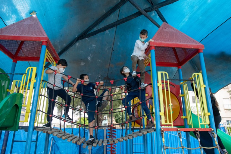 Children wearing masks play in a playground in Tel Nordau school, Israel