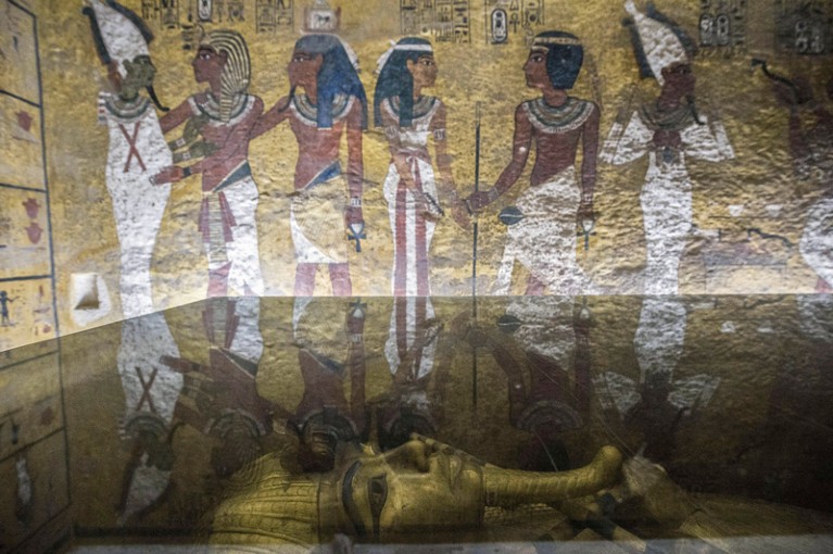 A low angle of King Tutankhamun's sarcophagus in his burial chamber, showing a mural on the wall.