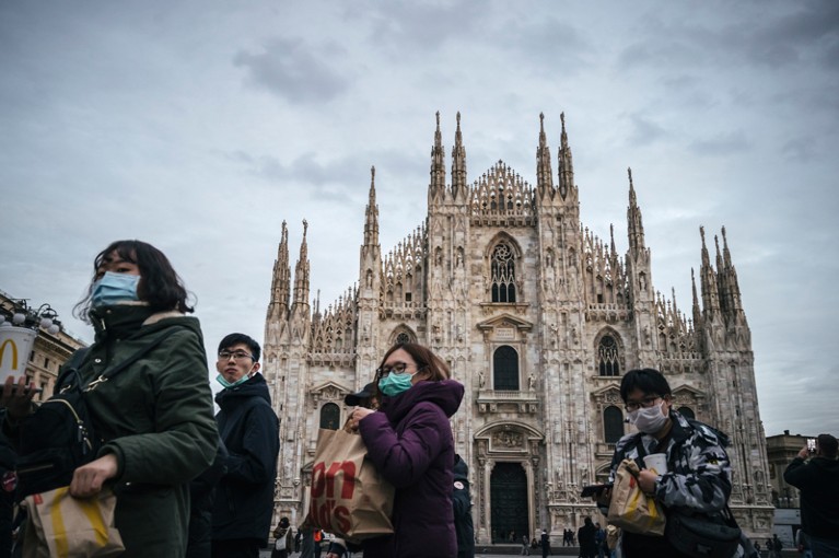 Tourists walk past the Duomo Cathedral in Milan wearing protective face masks.