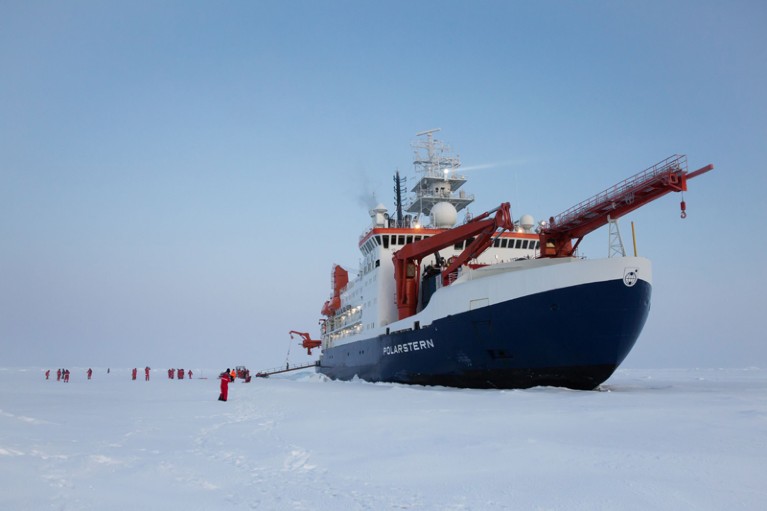 A large ship surrounded by ice. People are walking on the ice floe.