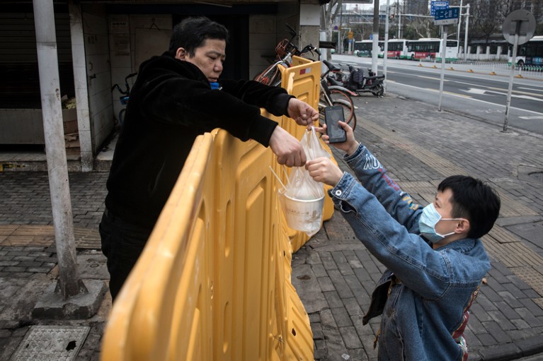 A man wearing a mask sells breakfast to nurses behind a makeshift barricade wall in Wuhan, China.