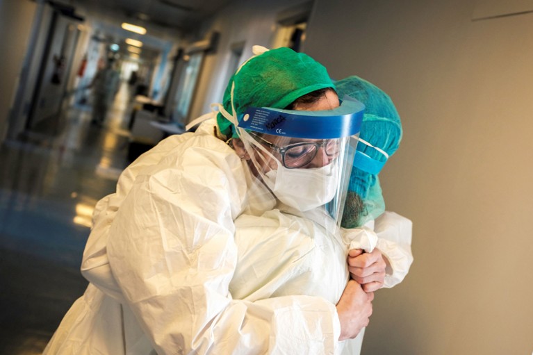 Nurses wearing protective mask and gear embrace in a hospital corridor