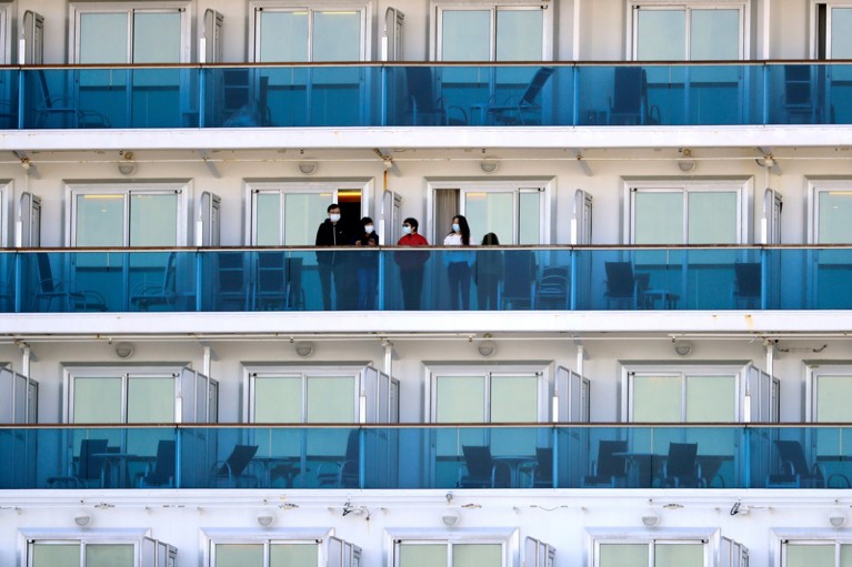 People in facemasks stand on balconies separated by partitions, surrounded by many empty balconies.