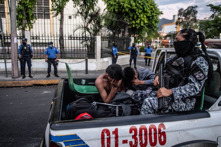 Two young men sit in the back of a police truck with an armed police officer after being arrested in San Salvador