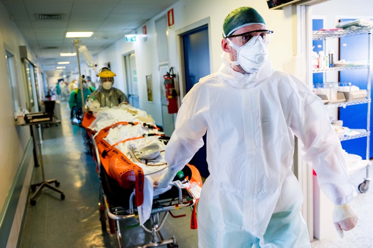 Medical workers in protective clothing and face masks transport a patient on a bed into a hospital in Cremona, Italy