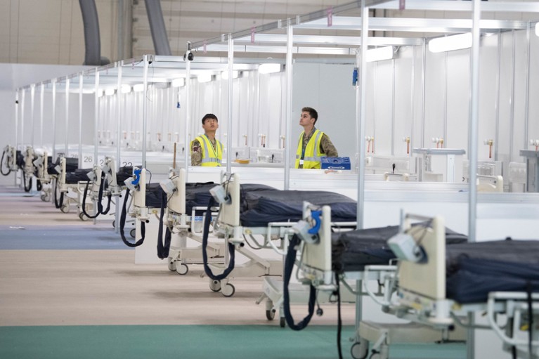Two men in high-vis vests stand amongst a row of beds in the newly built temporary hospital ward at London ExCel Centre
