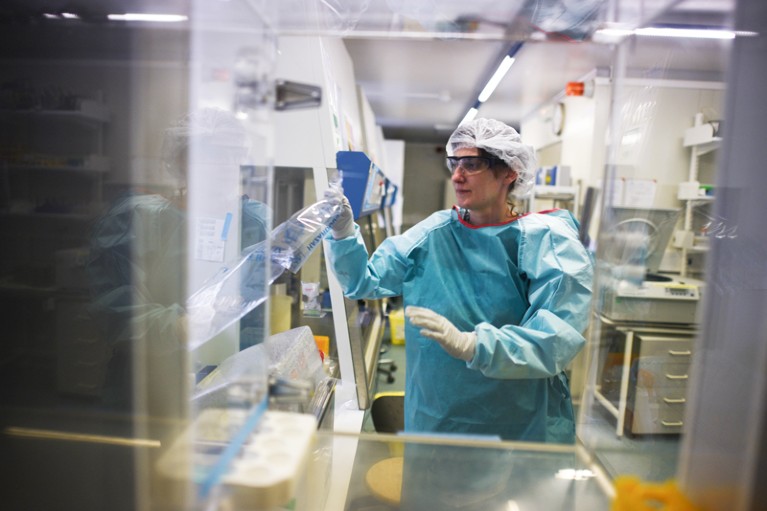 A researcher wears protective clothing while working a fume hood in a lab researching vaccines against Covid-19