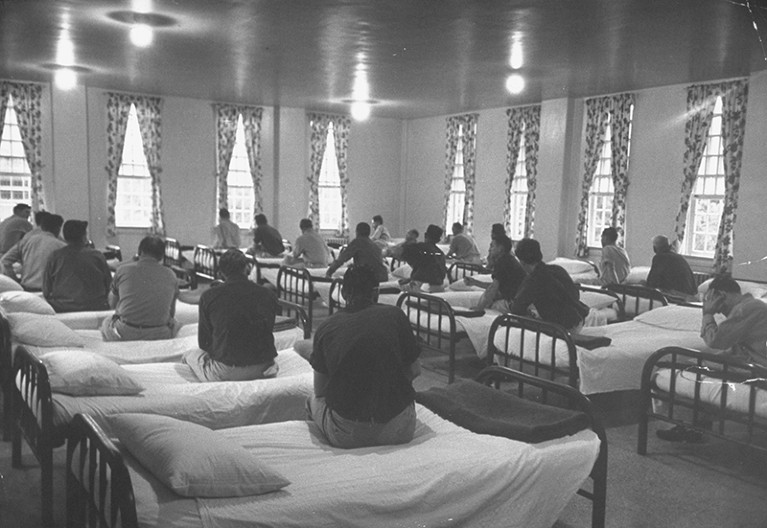 Patients sit on the edges of their beds and stare out of the windows in a dormitory at Milledgeville State Hospital