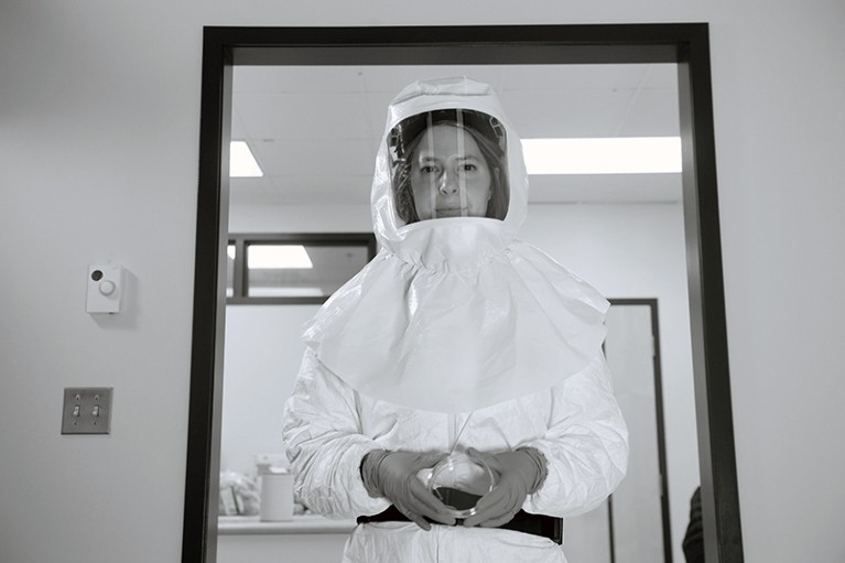 A woman in a full biohazard suit, photographed in black and white.