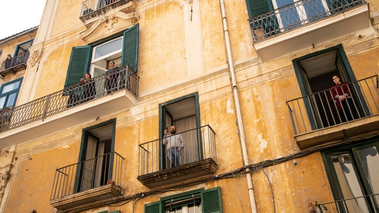 People standing on the balconies of an apartment block.