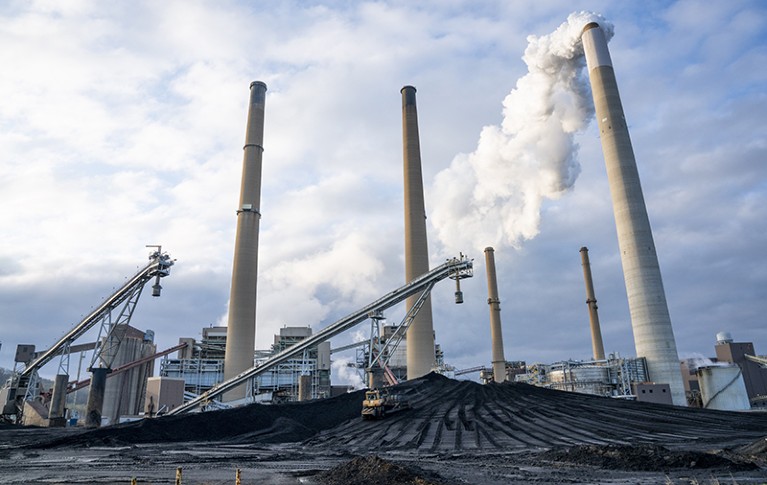 Coal is piled as emissions rise from a smoke stack at the Conesville Power Plant in Ohio, USA