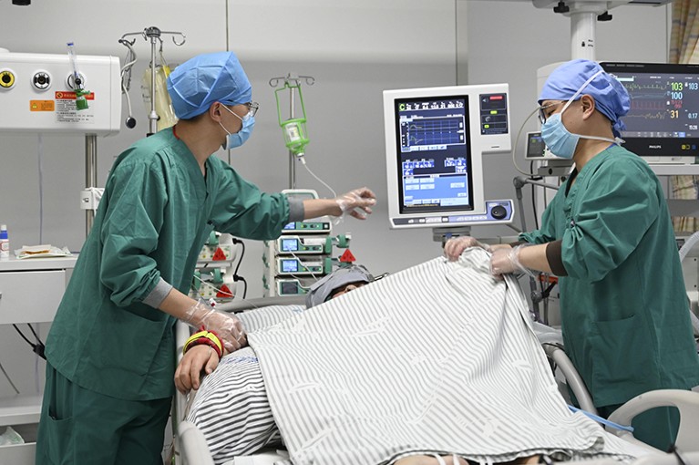 A patient in an intensive care unit receives treatment from two hospital workers.