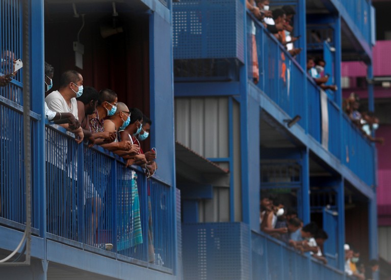 Groups of men wearing face masks lean over balconies.