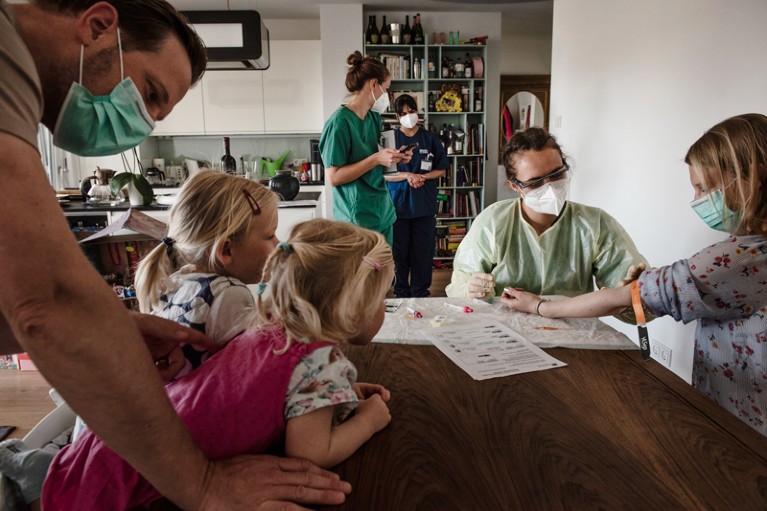 Health-care worker draw blood samples from a family wearing facemasks sitting at the dining table in their home in Munich