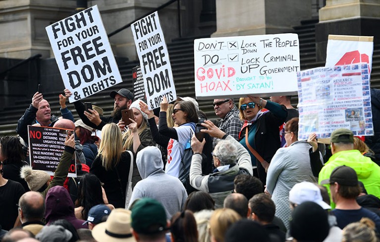 Anti-lockdown protesters hold placards on the steps of Victoria's state parliament in Melbourne