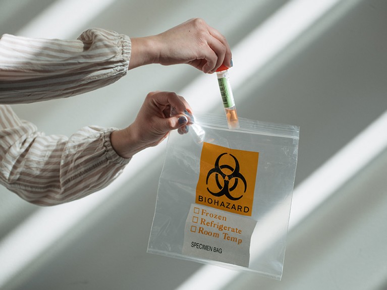 A research scientist puts a home sample test for novel coronavirus in a biohazard bag.