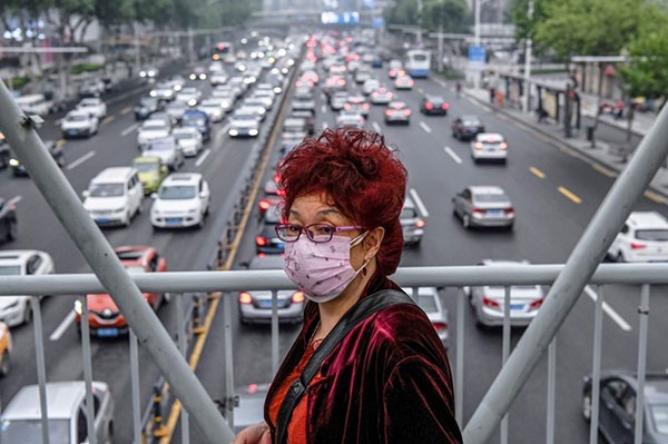 A woman wearing a facemask walks on a pedestrian bridge while traffic congestion is seen on a road in Wuhan