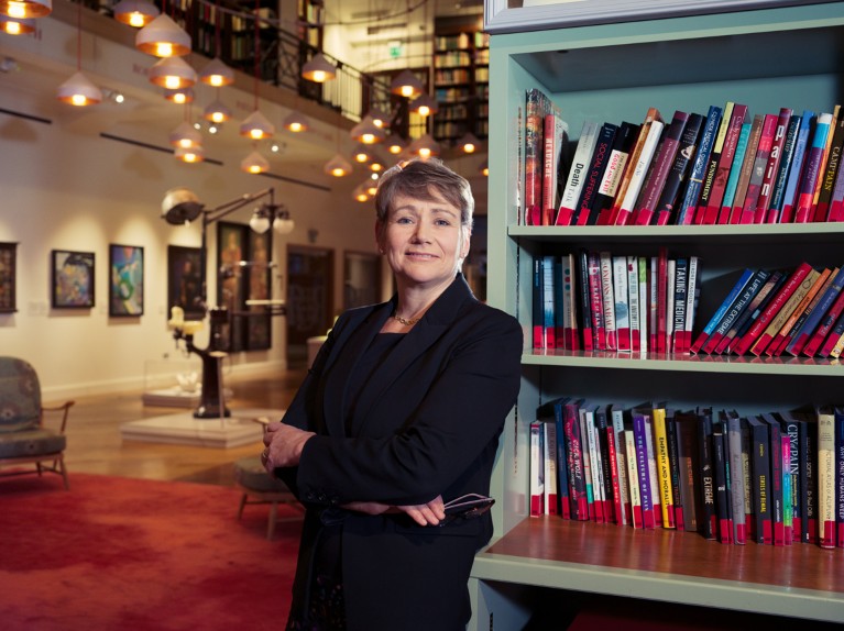 Anne-Marie Coriat posing for a portrait by a bookshelf in the Wellcome Reading Room, London.