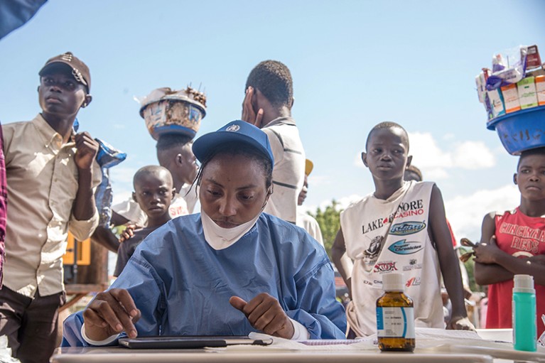A health worker records information on a tablet as people queue to be seen.