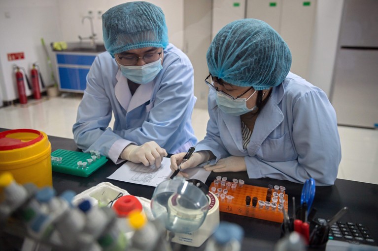 Two scientists in protective clothing work at a lab bench.