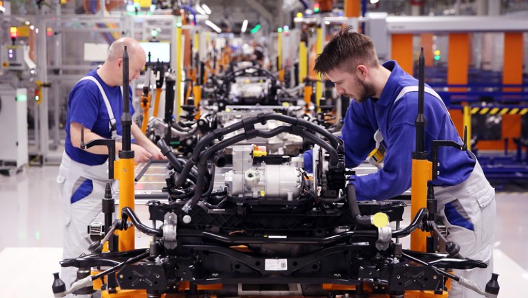 Workers at a car assembly line mount the lower body of an electric car including battery and charging port