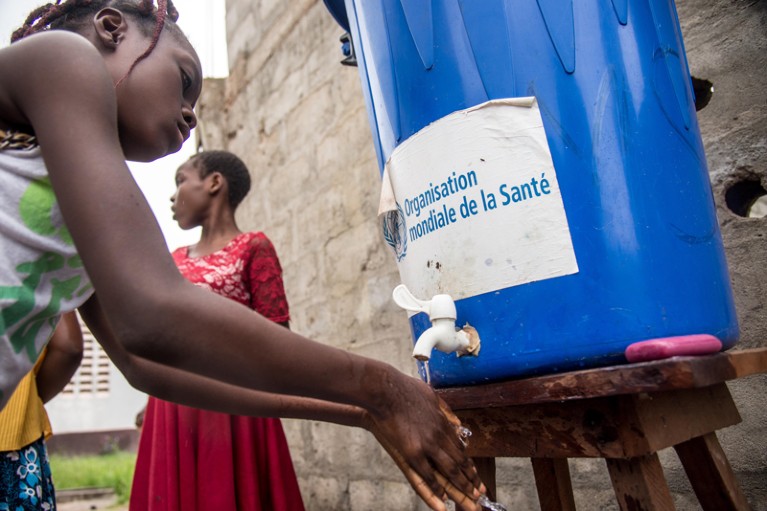 A woman washes her hands from a tank of water bearing a World Health Organization sticker in the Democratic Republic of Congo