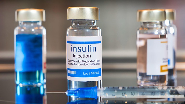 Bottle of Insulin injection with a syringe on black table and stainless steel background.