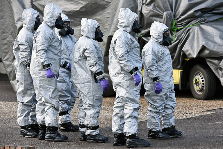 Persons in hazmat suits prepare to move a contaminated vehicle.