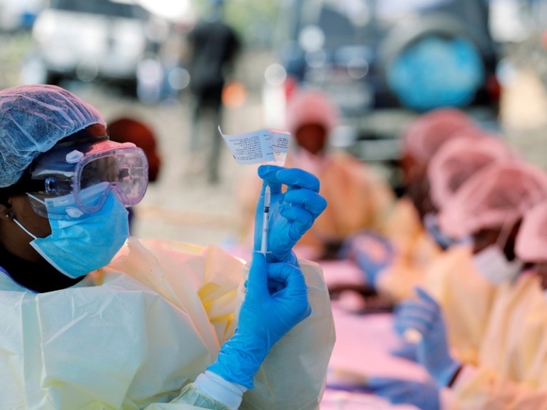 A health worker in protective gear and goggles prepares a syringe for a vaccination.