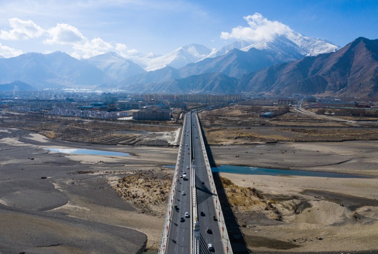 Aerial photo showing a motor way across a plateau with buildings and mountains in the background