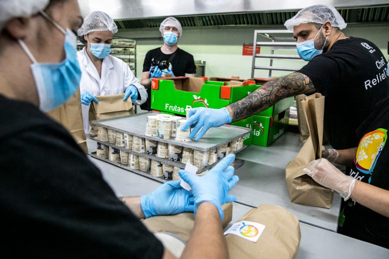 People in hair nets, face masks and gloves pack cartons into paper bags.