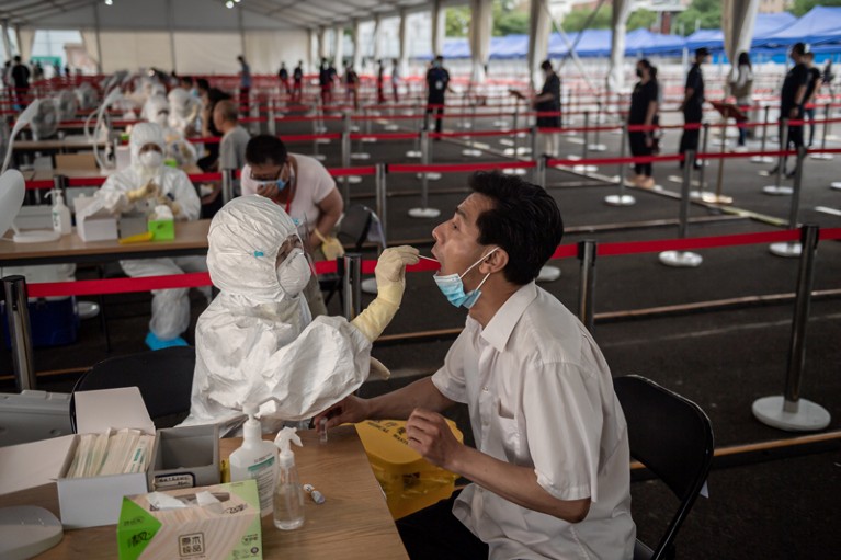 A health worker wearing a protective suit, face mask and face shield takes a swab test on a man