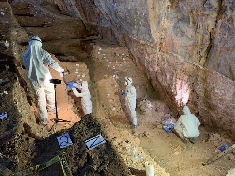 Researchers in protective clothing marking soil sample sites on multiple levels on a cave.