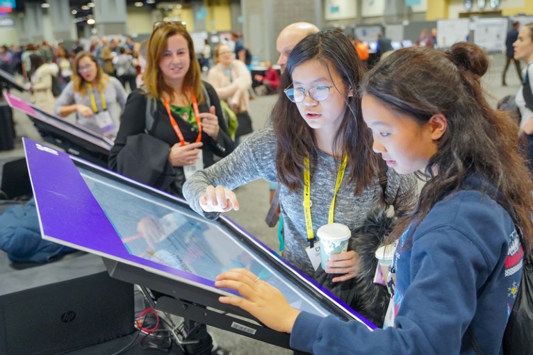 Two young female delegates at a science conference look at a touch screen display