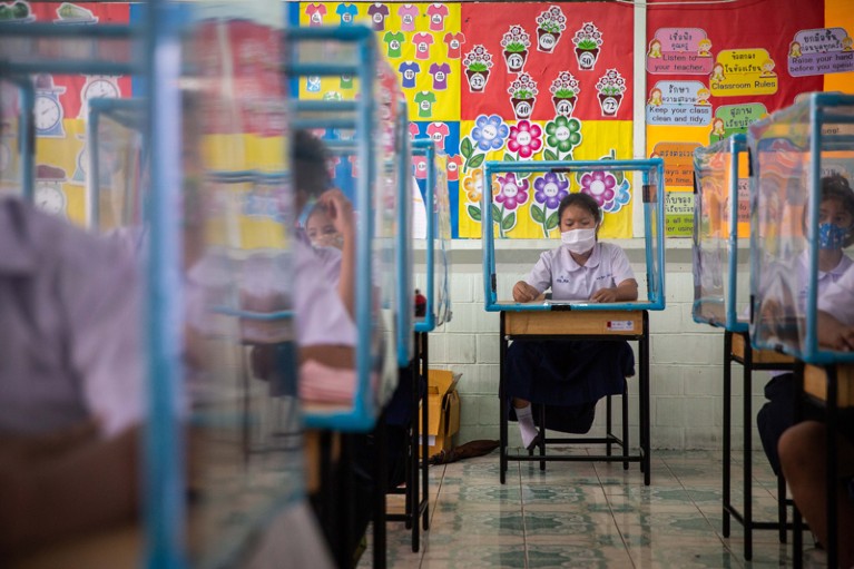 Thai school students wear face masks and sit at desks with plastic screens used for social distancing