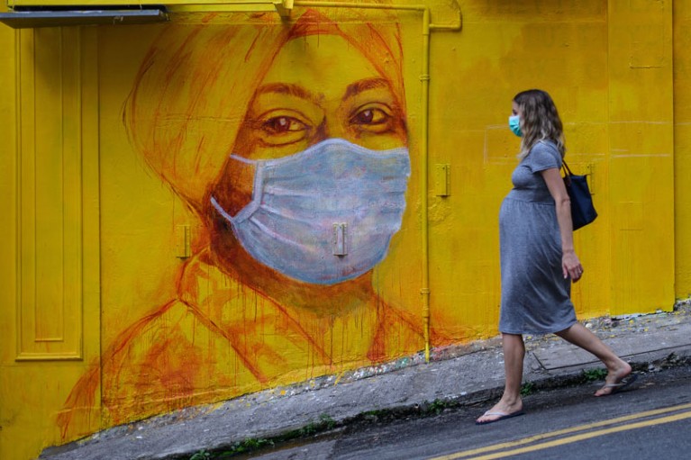 A pregnant woman wearing a face mask walks past a street mural in Hong Kong