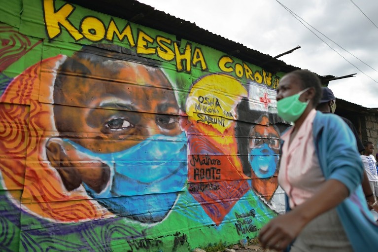 A woman wearing a face mask walks past a colourful mural of people wearing facemasks in Nairobi, Kenya