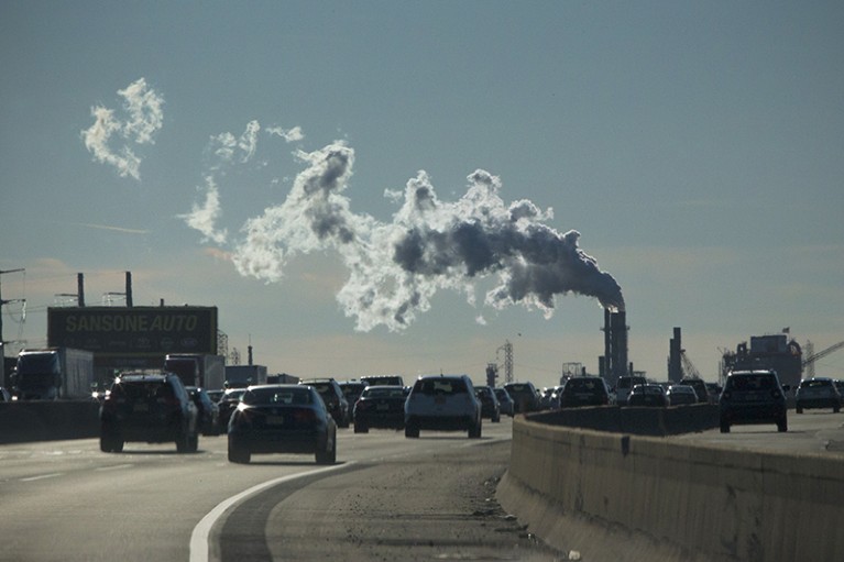 Cars on a turnpike pass a factory emitting smoke in New Jersey, U.S.