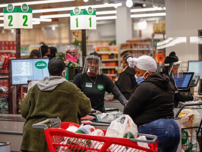 A cashier wearing a face shield talks with a customer at the Local Market Foods store in Chicago, April 2020.