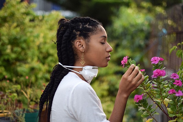 A young woman takes face mask off to smell the flowers