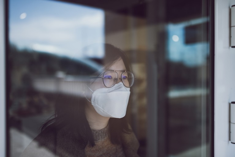 Woman looking through a window wearing a mask